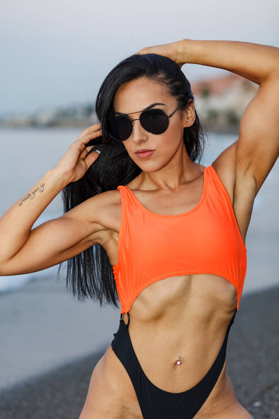 Fitness girl posing with a beautiful black and orange bikini - Photo, Image