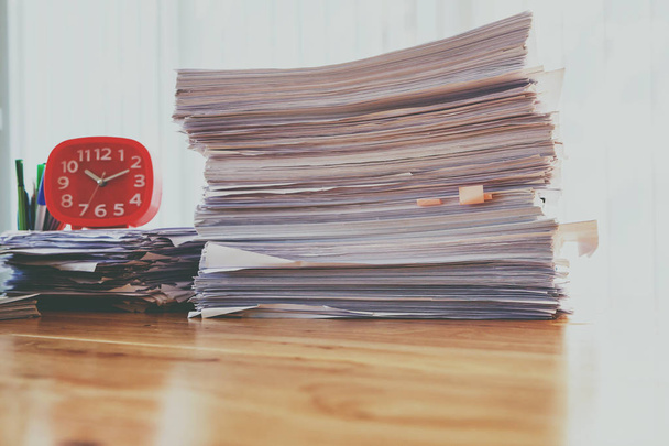Pino asiakirjoja punaisella kellolla ja toimistotarvikkeet pöydällä kotona toimistossa aamulla, lämmin sävy
 - Valokuva, kuva