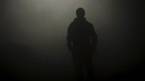 Silhouette nera dell'uomo in piedi nel buio fumoso. Filmati delle scorte. Misteriosa silhouette di giovane uomo sta nell'oscurità illuminata solo da fioca luce nella foschia
 - Foto, immagini