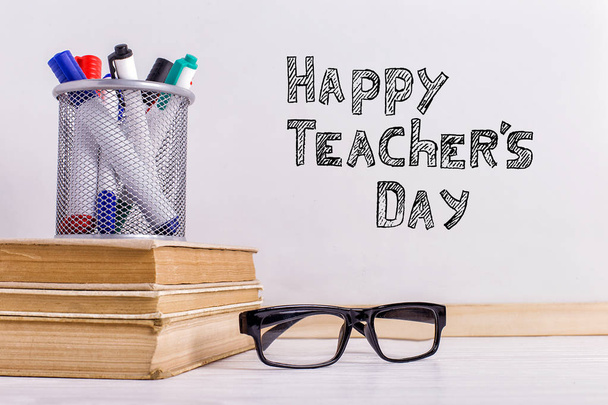 The inscription marker on a white board, Happy Teacher's Day. A table with books, glasses and attributes for writing. - Foto, Imagen