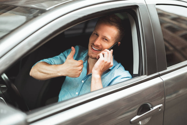 young handsome man drives unsafely having conversation on his smartphone on the run showing like sign - Foto, imagen