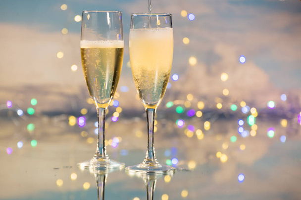 Serveren als een luxe mousserende Champagne in twee glazen bekers tegen een achtergrond verlicht door vele kleine lichten. Concept van viering. - Foto, afbeelding