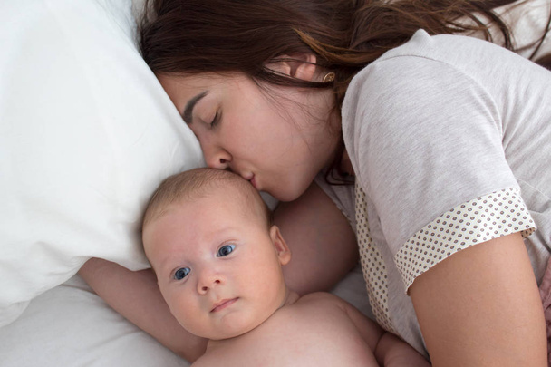 Beautiful brunette girl kissing her baby. They're in the bedroom - Fotografie, Obrázek