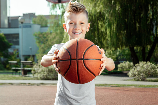 Portrait of a boy with a basketball on a basketball court. The concept of a sports lifestyle, training, sport, leisure, vacation. - Photo, image