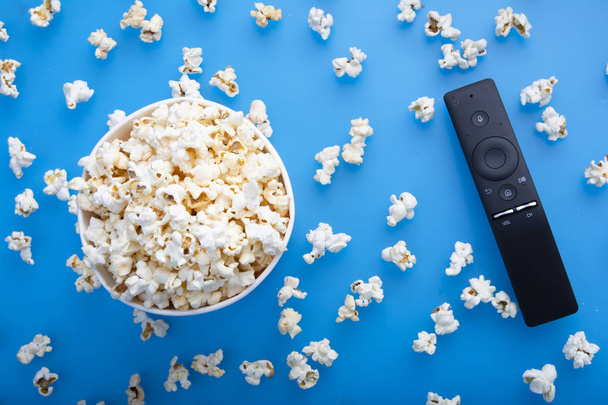 Close-up of remote control and testy warm popcorn viewed from above on blue background. The concept of watching a movie, TV, DVD. Entertainments - Fotó, kép