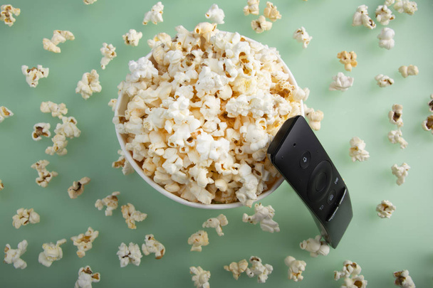 Spilled popcorn on green background with TV remove. Cinema, movies and entertainment concept. Top view. - Fotoğraf, Görsel