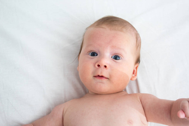 The surprised baby lies on a white blanket. The concept of inter - Zdjęcie, obraz