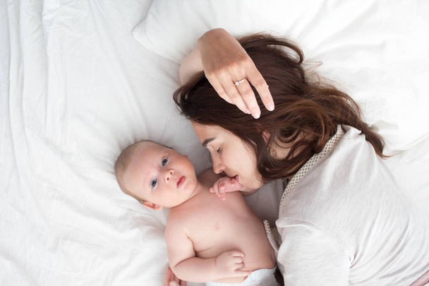 Beautiful brunette girl kissing her baby. They're in the bedroom - Фото, изображение