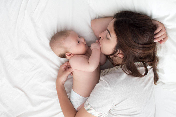Beautiful brunette girl kissing her baby. They're in the bedroom - Foto, imagen
