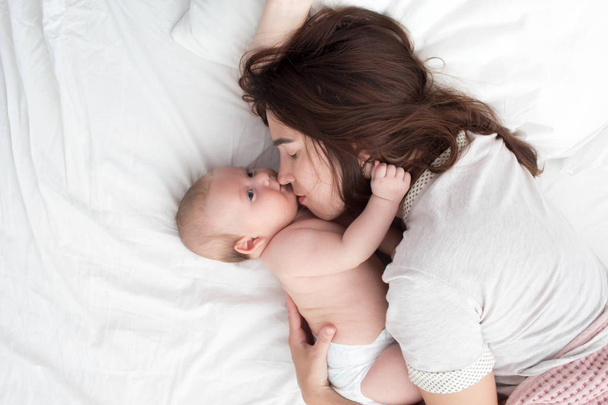 Beautiful brunette girl kissing her baby. They're in the bedroom - Φωτογραφία, εικόνα