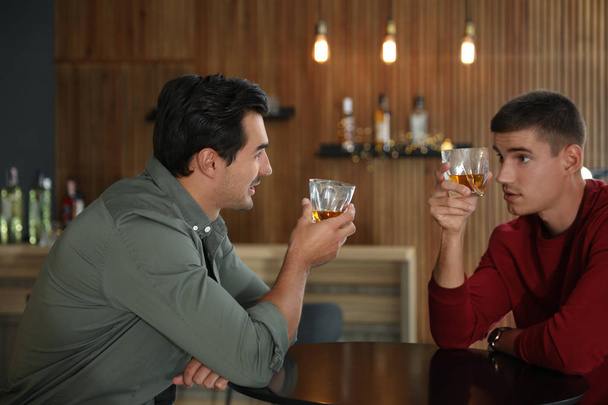 Young men drinking whiskey together in bar - Foto, imagen