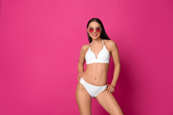 Beautiful young woman in white bikini with sunglasses on pink background. Space for text - Zdjęcie, obraz