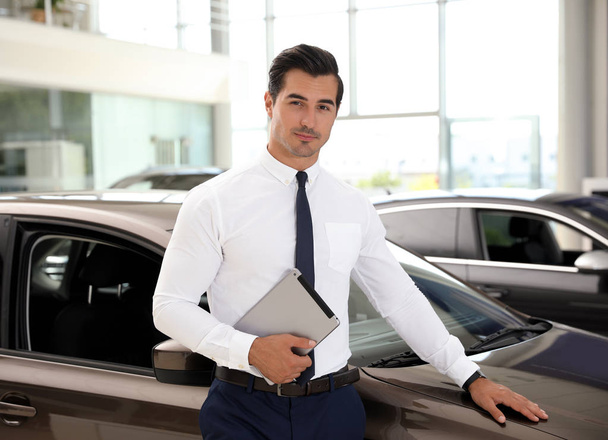 Young salesman with tablet near car in modern dealership - Photo, image
