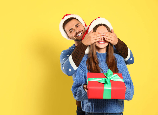 Couple portant des pulls de Noël et des chapeaux de Père Noël sur fond jaune
 - Photo, image