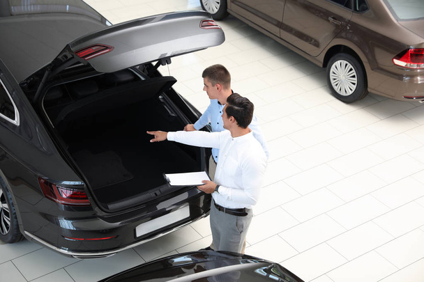 Young salesman working with client in modern car dealership, above view - 写真・画像