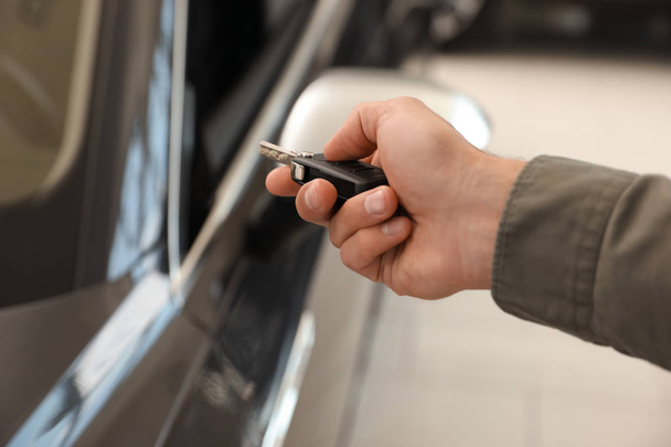 Young man checking alarm system with car key indoors, closeup - Zdjęcie, obraz