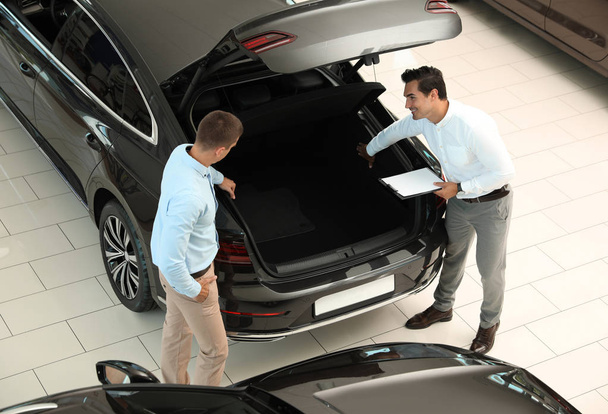 Young salesman working with client in modern car dealership, above view - Photo, image