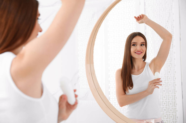 Beautiful young woman applying deodorant in bathroom - 写真・画像