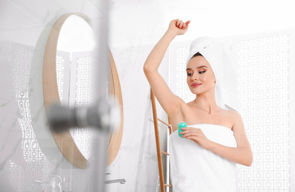 Beautiful young woman applying deodorant after shower in bathroom. Space for text - Photo, Image