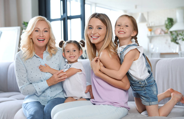 Молодая женщина со зрелой матерью и маленькими дочерьми в гостиной
 - Фото, изображение