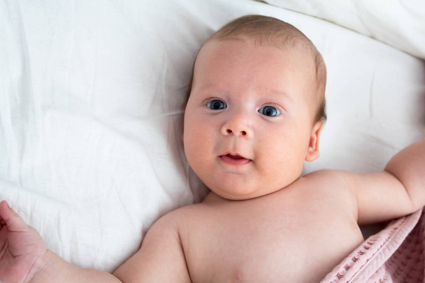 The surprised baby lies on a white blanket. The concept of inter - Photo, image