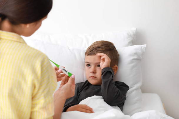 Mother measuring temperature of her sick son in bed - Foto, immagini
