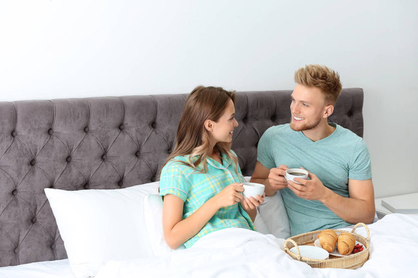 Happy young couple having romantic breakfast in bed at home - Фото, зображення