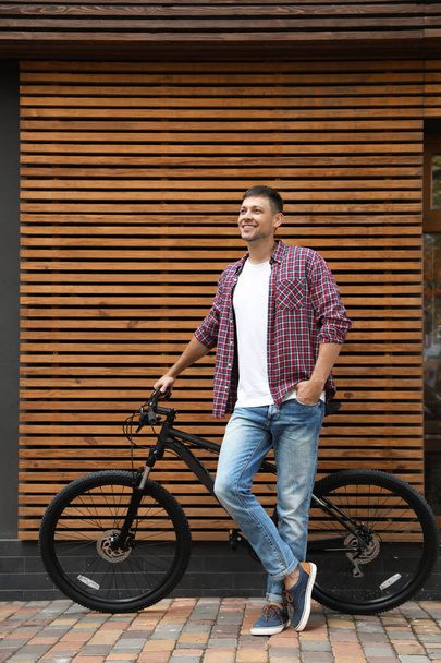 Handsome man with modern bicycle near building outdoors - Foto, Imagem