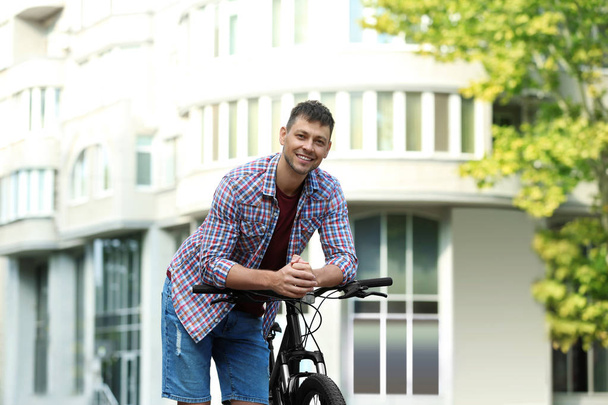 Handsome man with modern bicycle on city street - Фото, изображение