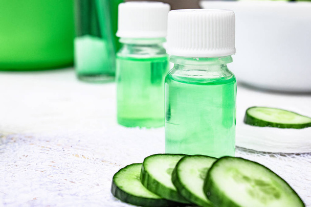 Sliced cucumber and a bottle of cucumber extract on a white wooden table and a white background. Liquid cosmetics for skin care. - Foto, Bild