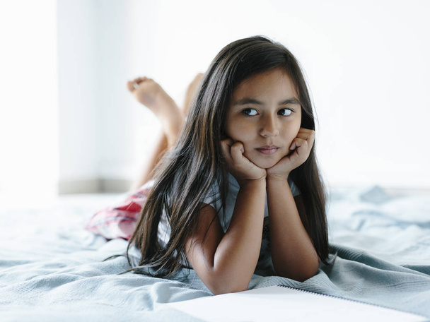 Mladá dívka ležící na posteli a dívá se doleva. - Fotografie, Obrázek