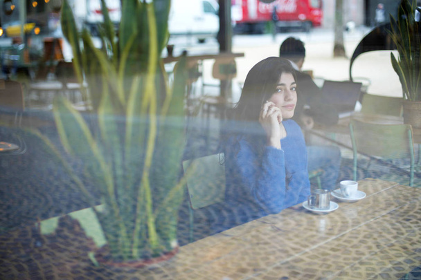 Woman talking on smart phone while sitting in cafe seen through window - Fotoğraf, Görsel