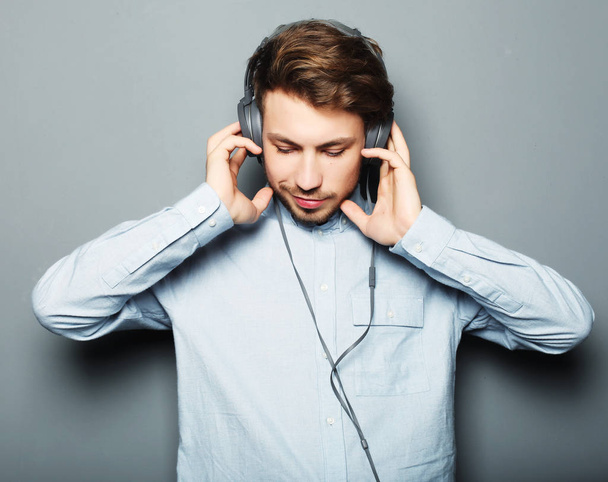 life style, happiness, emotional and people concept: Enjoying his favorite music. Happy young stylish man adjusting his headphones - Foto, afbeelding