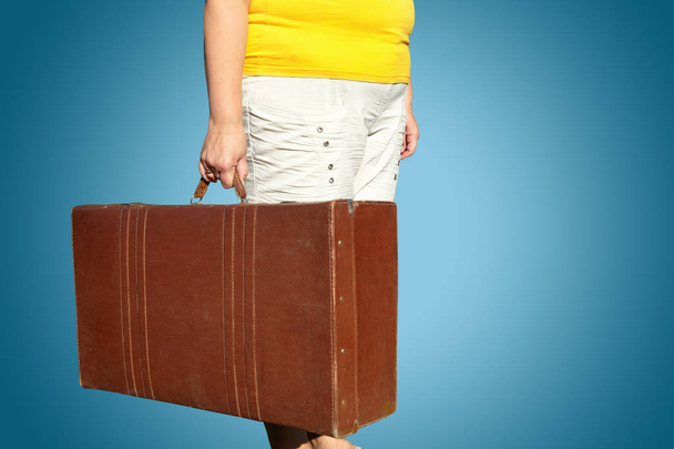 Woman in a yellow T-shirt stands with a suitcase in her hand - Fotó, kép