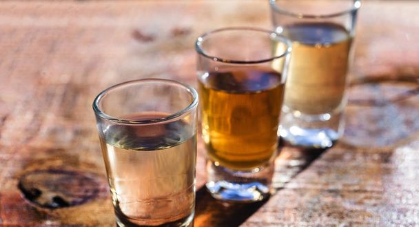tři skleněné brýle z brazilského zlata a bílého cachaca izolované na rustikálním dřevěném pozadí. Typický nápoj z Brazílie. - Fotografie, Obrázek
