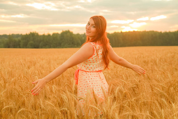 girl in dress walking in golden ripe wheat field at sunset - Foto, immagini