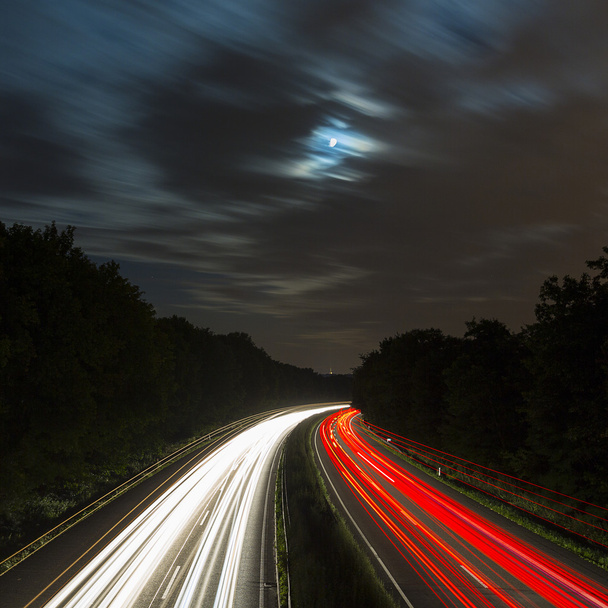 μεγάλη έκθεση χρόνου αυτοκινητόδρομος πλεύσης αυτοκίνητο φως μονοπάτια ραβδώσεις της ταχύτητα του φωτός στον αυτοκινητόδρομο φεγγάρι θολό - Φωτογραφία, εικόνα