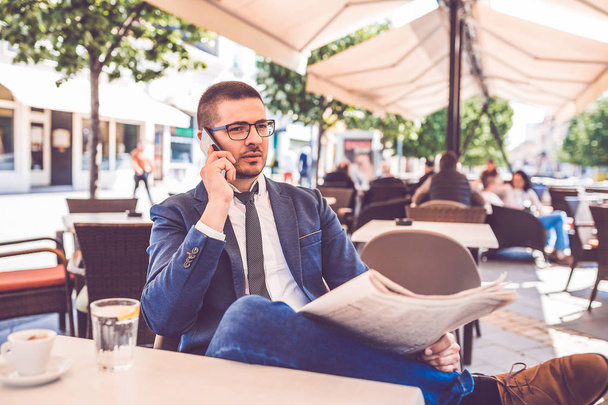 Young businessman reading newspapers and talking on mobile phone - Photo, Image