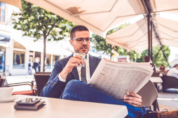 Jonge man met glas water in de hand lezing krant bij elkaar overtreffen - Foto, afbeelding