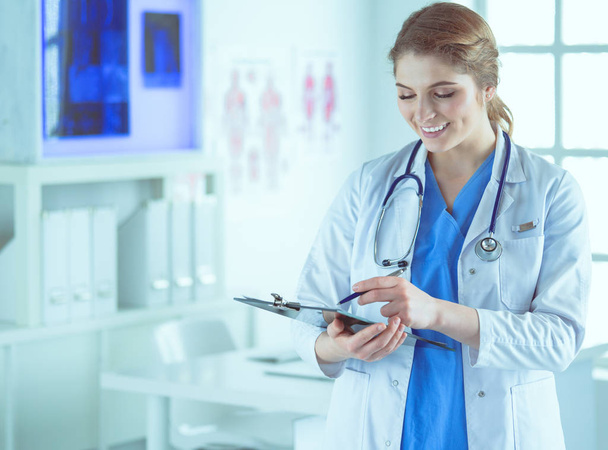 Doctor with a stethoscope, holding a notebook in his hand. Close-up of a female doctor filling up medical form at clipboard while standing straight in hospital - Foto, Imagen