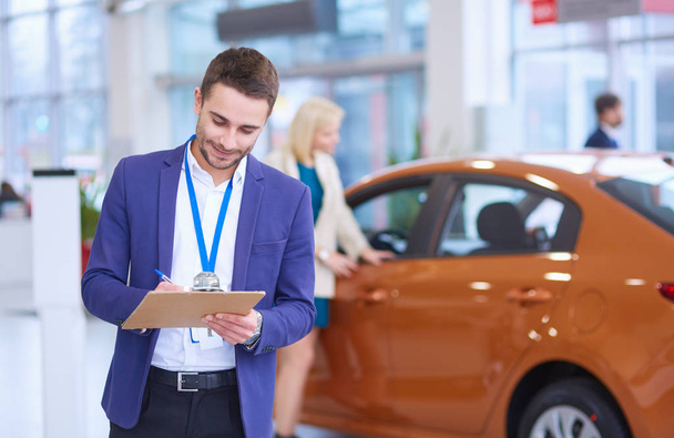 Dealer with woman stands near a new car in the showroom - Foto, imagen