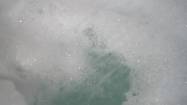 A stream of water from the shower blurs a bunch of foam into the bathtub. Bubbles form and fall. Use of hygiene products - Záběry, video