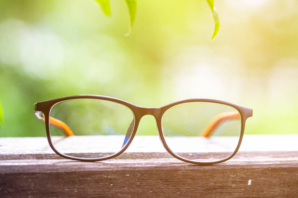 Close up beautiful vintage black and brown eye glasses with shiny black frame on wooden table over colorful outdoor blurred greenery nature background with copy space. Conceptos de visión y salud
. - Foto, imagen