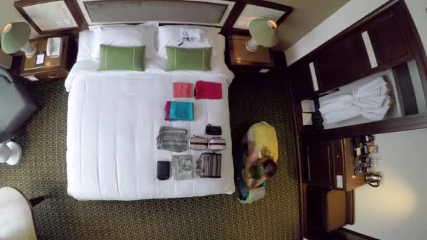 Von oben nach unten, Zeitraffer: Die junge Frau packt ihre Reisetasche mit der Kleidung und verlässt das Hotelzimmer. Blick von oben auf Touristinnen, die ihr Gepäck für die Abreise aus ihrer Ferienwohnung in Vietnam vorbereiten - Filmmaterial, Video