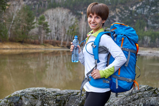 Walking smiling young woman with bottle of water and backpack. Outdoor sports portrait - Foto, immagini