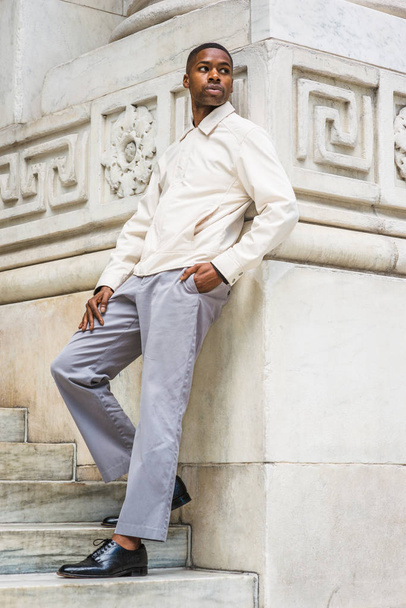 New York'ta Genç Yakışıklı Afro-Amerikan Adam Portresi. Genç siyah adam açık renkli ceket giyiyor, gri pantolon, siyah deri ayakkabı, vintage mermer duvara karşı duran, etrafa bakan, relaxin - Fotoğraf, Görsel
