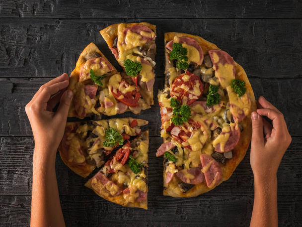 Baby's hands and fresh homemade pizza on a black wooden table. The view from the top. - Foto, imagen