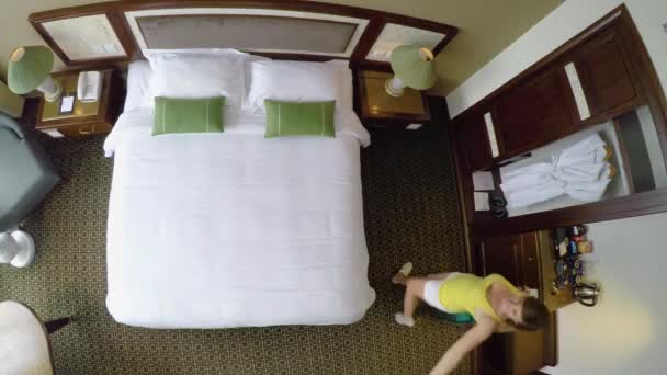TOP DOWN: turista feminina brincalhão cai na cama confortável em seu apartamento de férias de luxo no Vietnã. Mulher caucasiana alegre traz sua bagagem na suíte de férias e pula para a cama grande
. - Filmagem, Vídeo