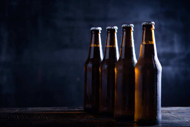 Glazen flessen bier met glas en ijs op donkere achtergrond - Foto, afbeelding