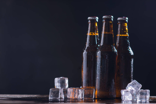 Szklane butelki piwa ze szkłem i lodem na ciemnym tle - Zdjęcie, obraz